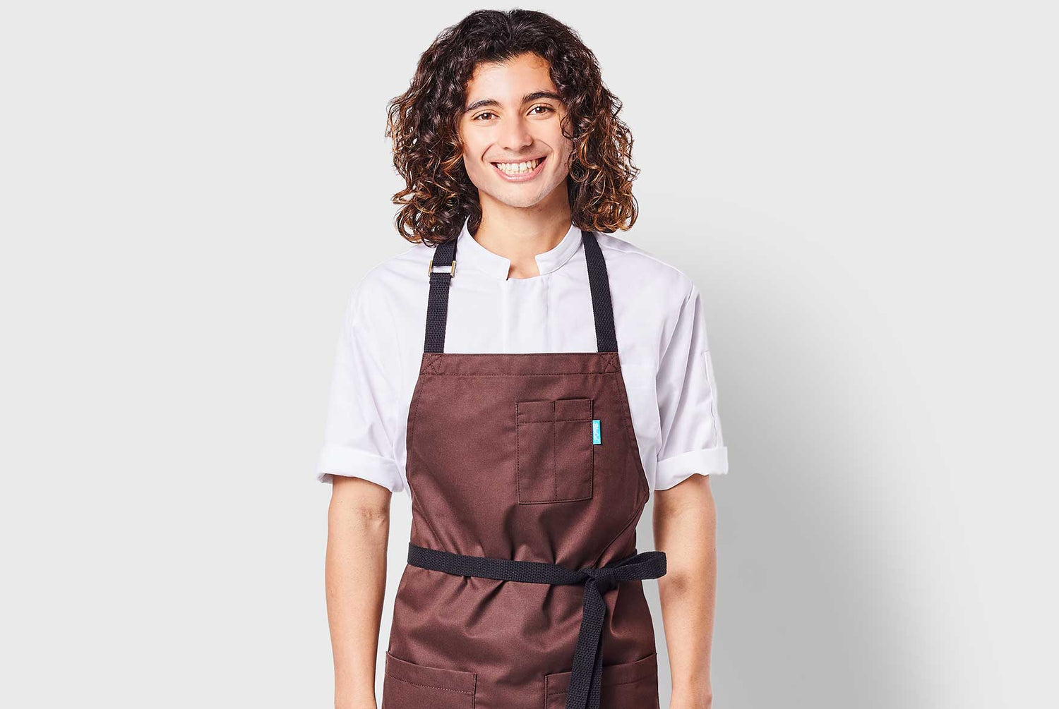 Image of person wearing a Line apron in cacao with a Greyson chef coat in white.