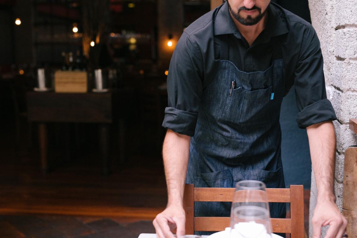 A restaurant employee in a sharp apron, setting the table for potential customers