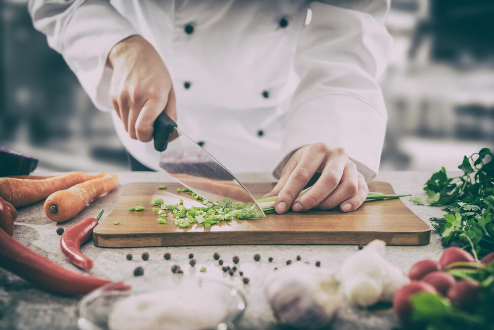 Professional chef cutting green onions on cutting board in a professional kitchen setting.