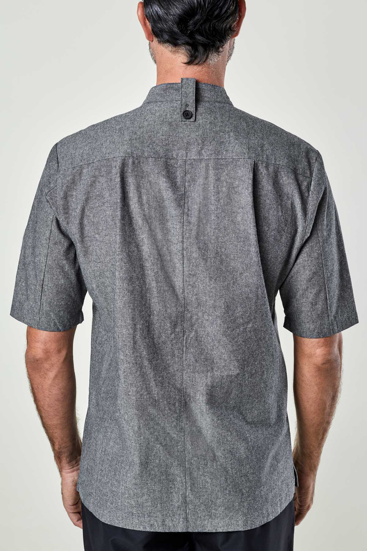 back view of a man wearing a charcoal chambray double-breasted chef coat.