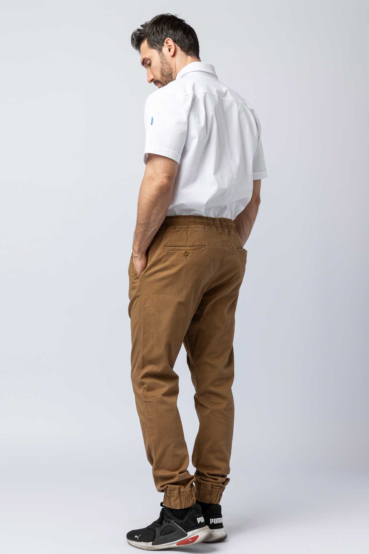 Rear view of a man wearing khaki joggers and a white work shirt.