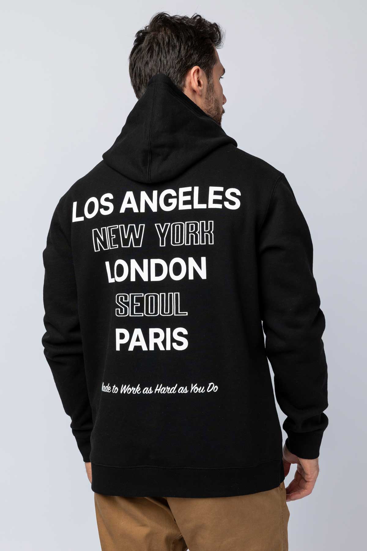 Rear view of a man wearing a black hoodie with major cities printed on the back.
