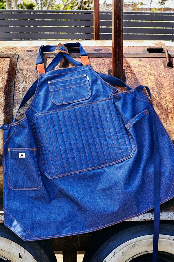 Blue denim Pitmaster Apron on a smoker with a rustic background