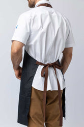 Rear view of a man wearing a navy waxed canvas apron.