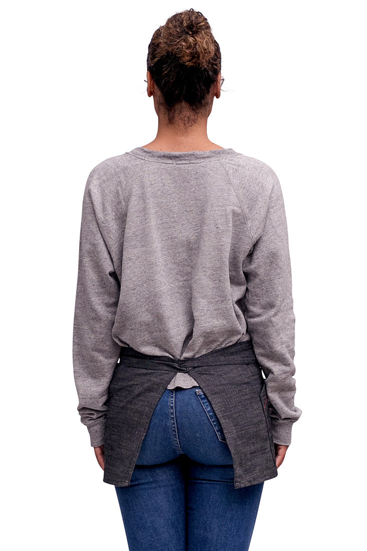 A back view of person wearing a charcoal mini denim apron standing against a neutral background.