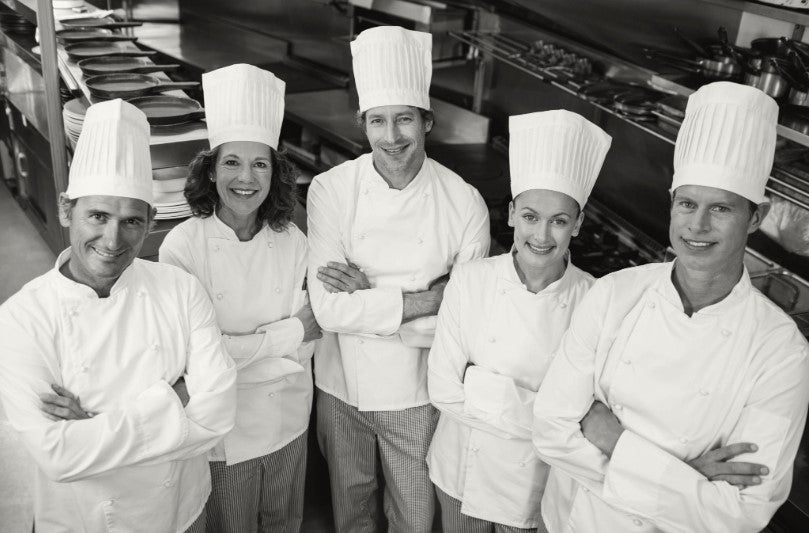 A group of chefs smiling while standing in a kitchen. 