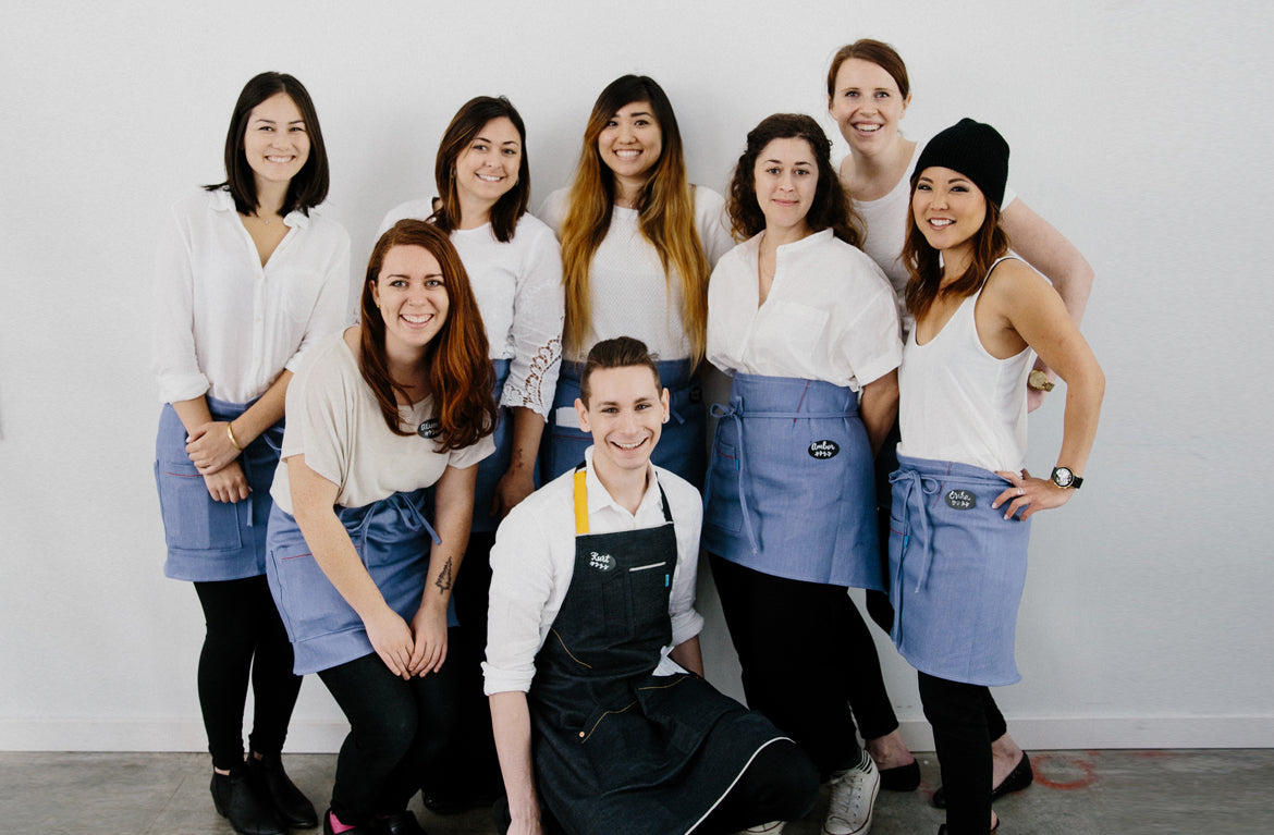 FOH staff wearing coordinated waist aprons and a bib apron.