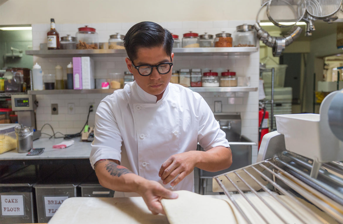 A chef in a clean white BlueCut professional chef coat preparing dough in a commercial kitchen.