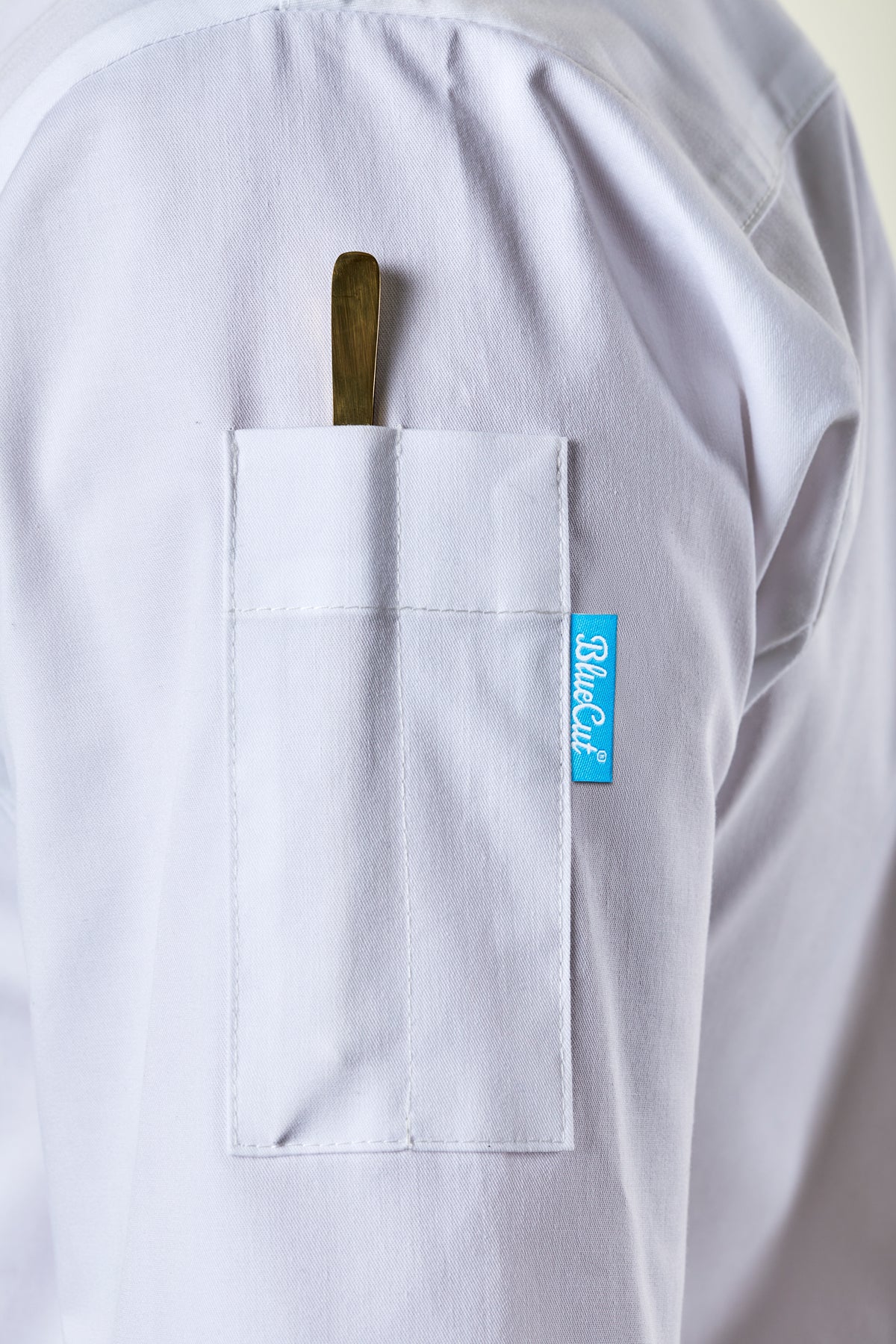 White chef coat with a  pen pocket and a BlueCut label on a light background