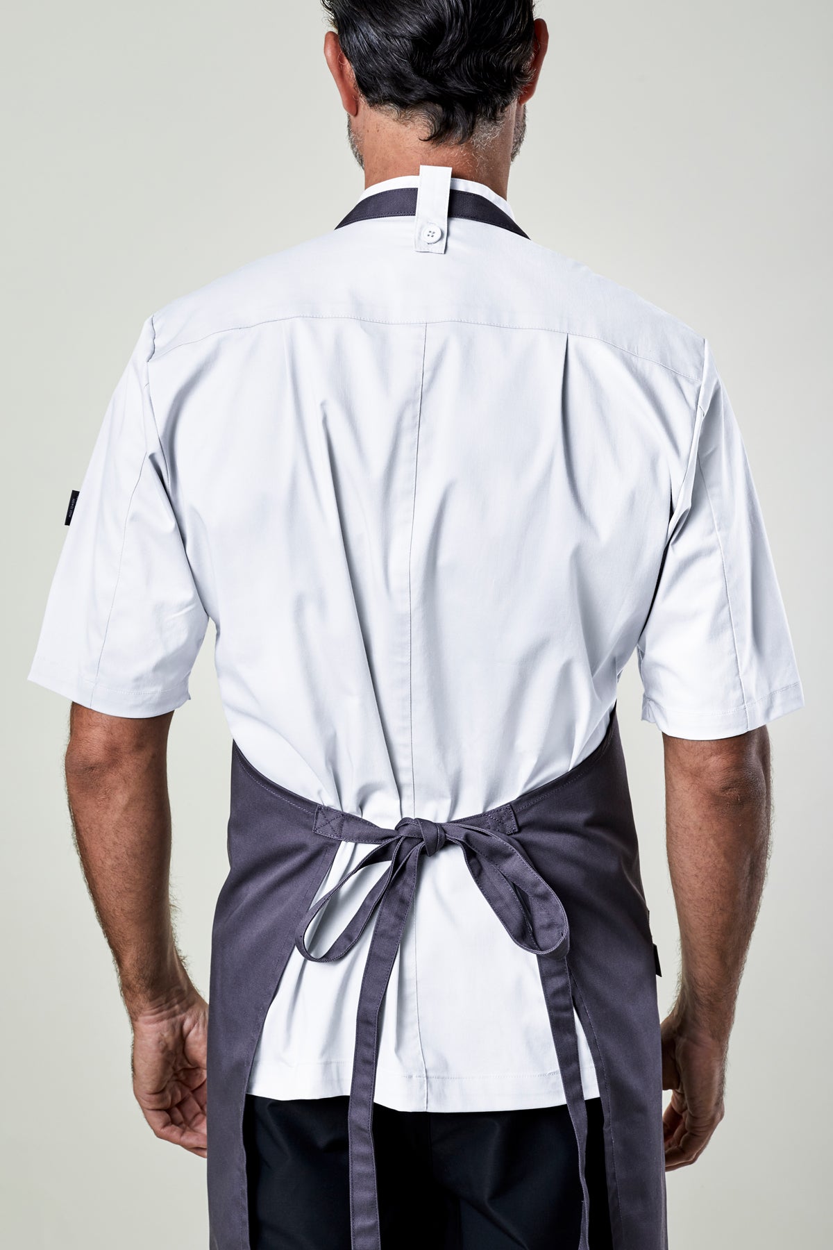 Back view of a man wearing a white shirt and gray apron on a plain background