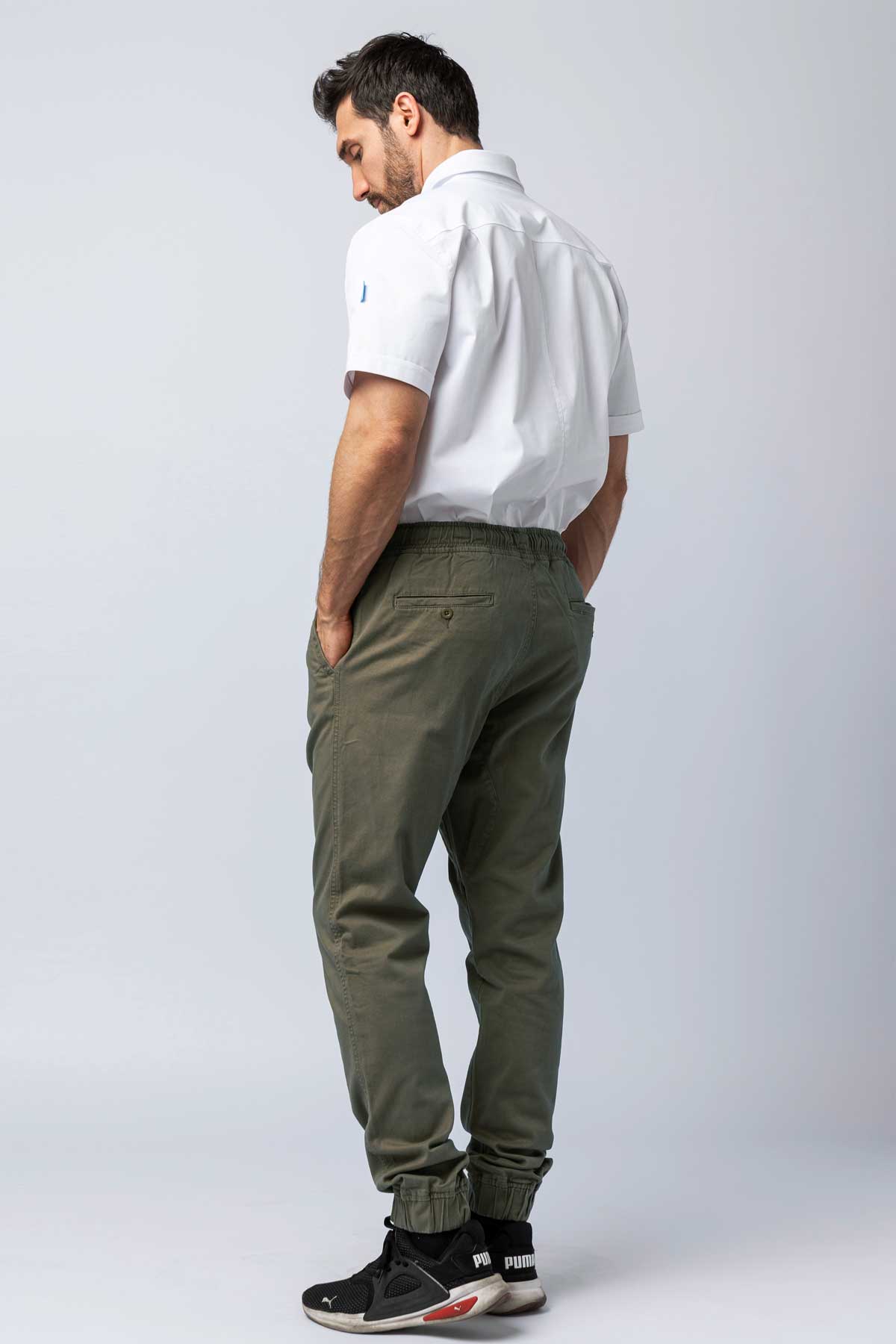 Rear view of a man wearing olive joggers and a white work shirt.