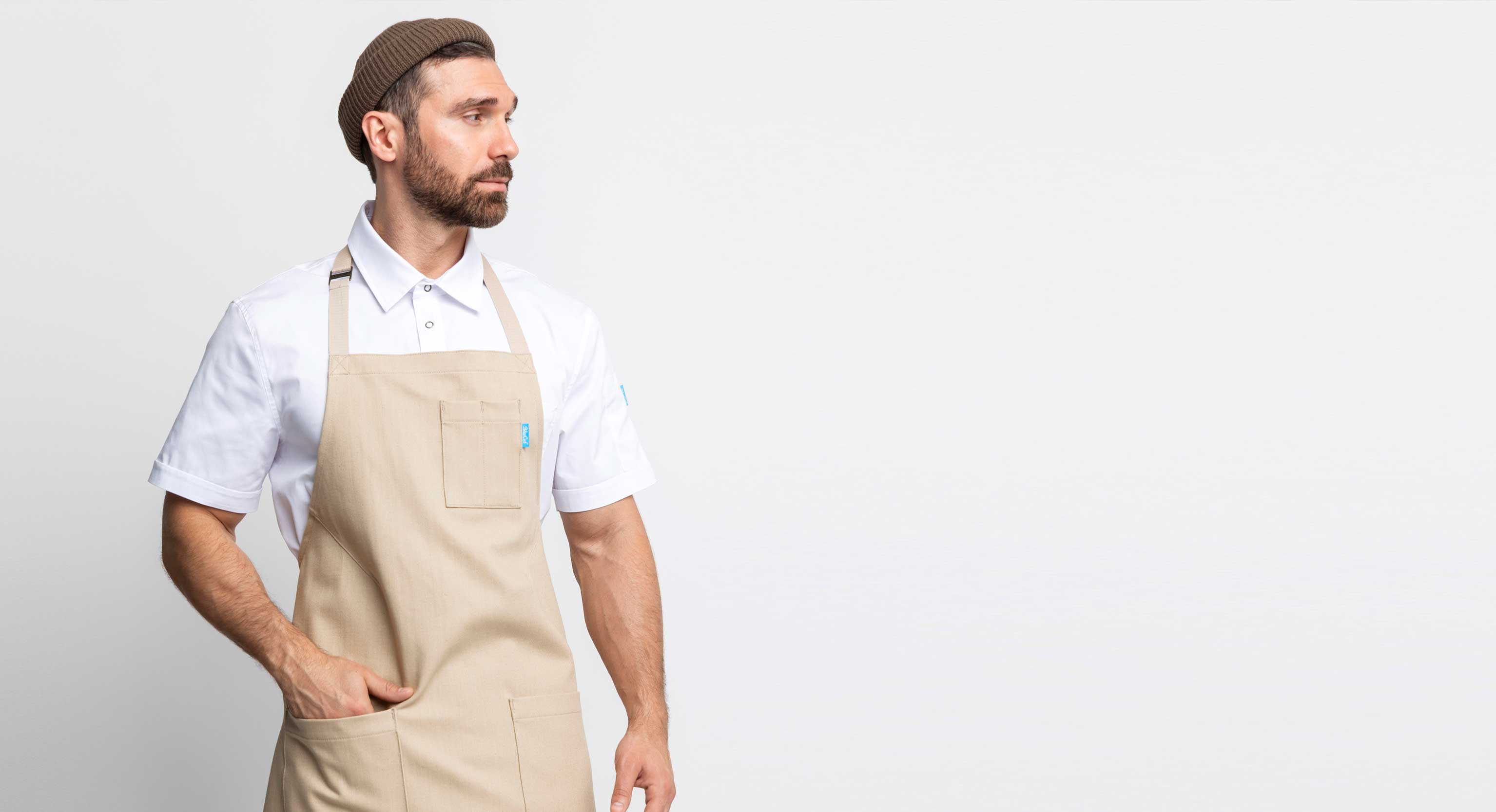 Man wearing a beige apron over a white shirt on a plain background
