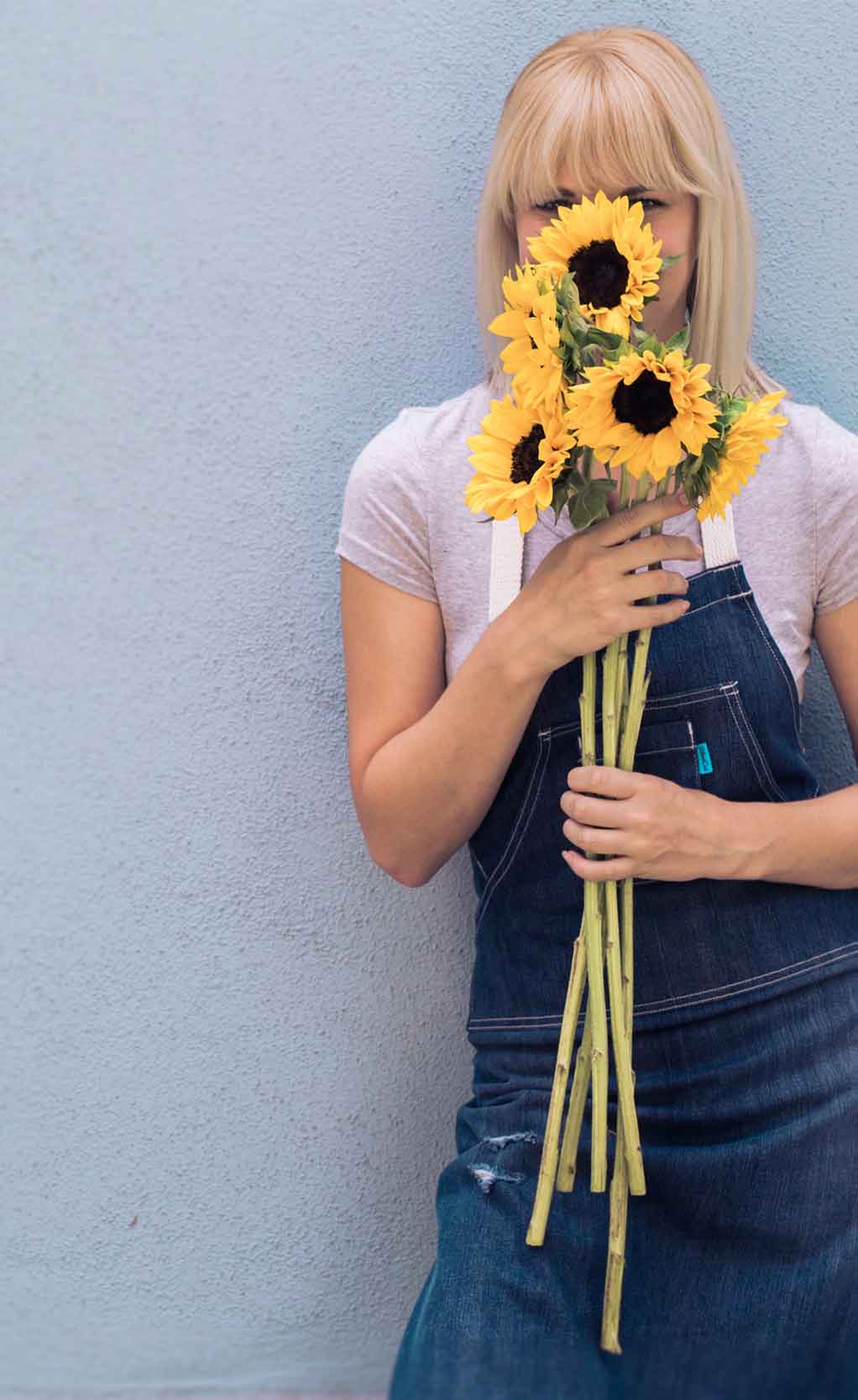 Image of women wearing denim apron and holding sunflowers