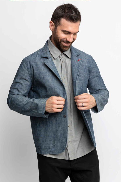 Man looking down while buttoning a blue chambray task jacket.