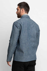 Three-quarter rear view of a man wearing a blue chambray task jacket.