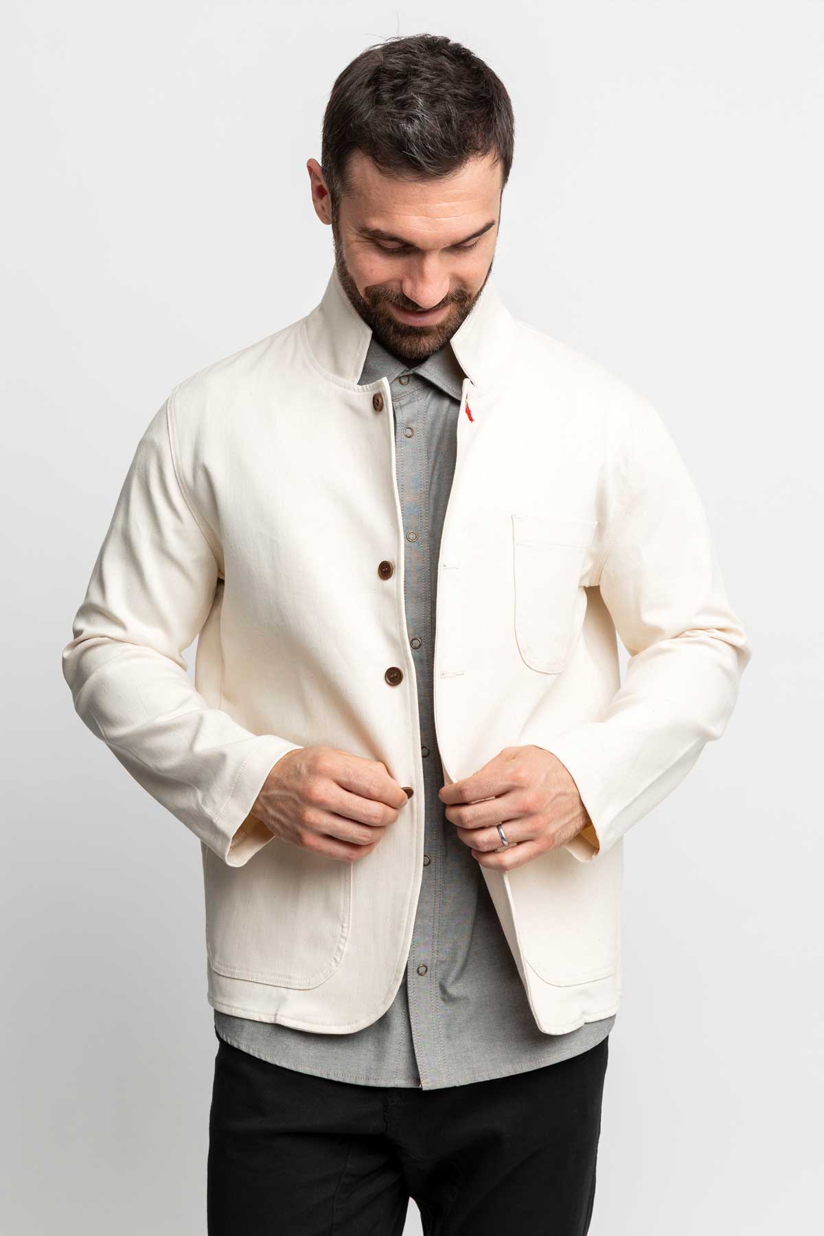Man looking down while buttoning a natural-colored task jacket.